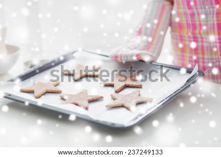 christmas, food, holidays and people concept - close up of woman in apron and oven glove with cookies on oven tray
