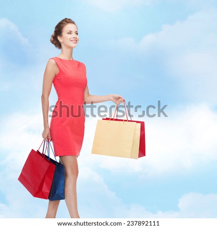 shopping, sale and holidays concept - smiling elegant woman in red dress with shopping bags over blue cloudy sky background