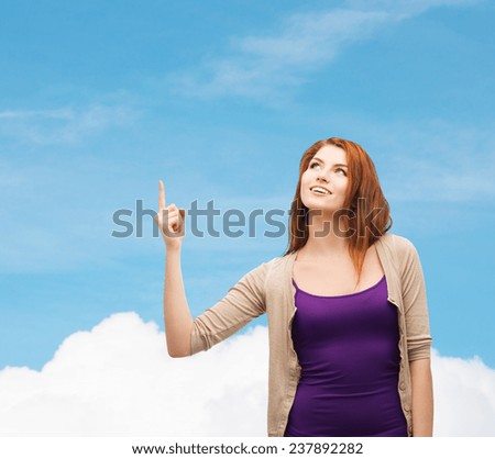 future, dream, gesture and people concept - smiling teenage girl in casual clothes pointing finger up over blue sky and cloud background