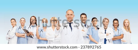 medicine, profession, teamwork and healthcare concept - international group of smiling medics or doctors with clipboard and stethoscopes with showing thumbs up over blue background