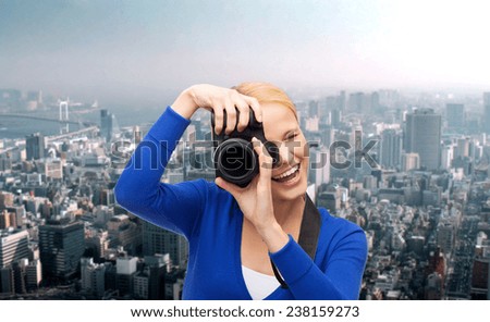 photography, technology and people concept - smiling young woman taking picture with digital camera over city background