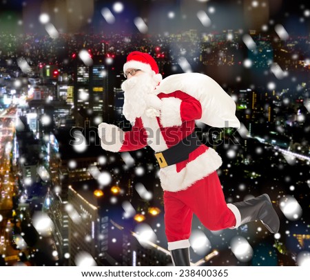 christmas, holidays and people concept - man in costume of santa claus running with bag over snowy night city background