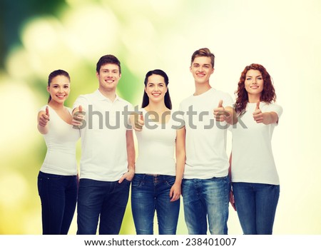 advertising, ecology, nature, friendship and people concept - group of smiling teenagers in white blank t-shirts showing thumbs up over green background