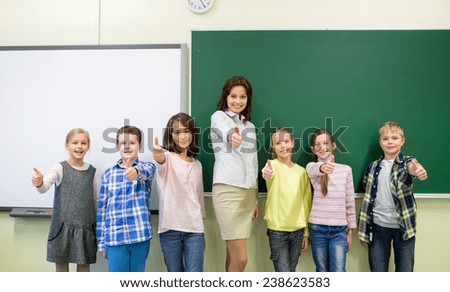 education, elementary, gesture and people concept - group of school kids and teacher showing thumbs up in classroom