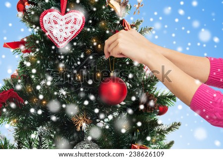 winter holidays, celebration and people concept - close up of woman hands decorating christmas tree with ball over blue background with snow