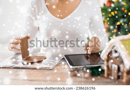 cooking, people, christmas and technology concept - close up of woman with tablet pc computer making gingerbread houses at home