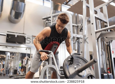 sport, bodybuilding, equipment and people concept - young man with barbell flexing muscles on t-bar row machine in gym