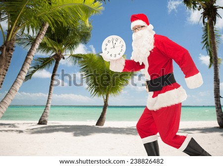 christmas, holidays and people concept - man in costume of santa claus running with clock showing twelve over tropical beach background
