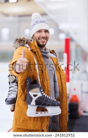 people, sport, gesture and leisure concept - happy young man with ice-skates showing thumbs up on skating rink