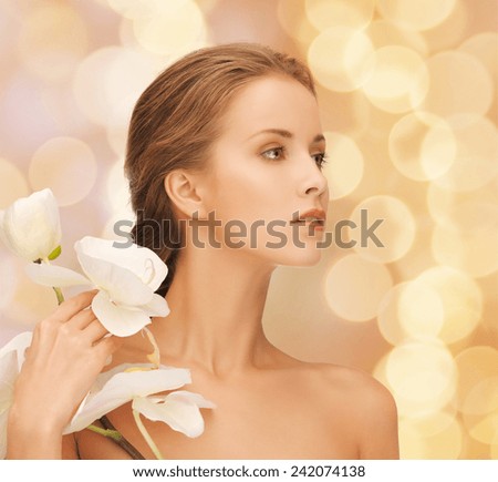 beauty, people and health concept - beautiful young woman with orchid flowers and bare shoulders over beige lights background
