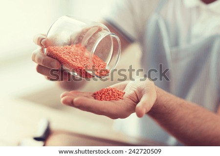 cooking and home concept - close up of male emptying jar with red lentils