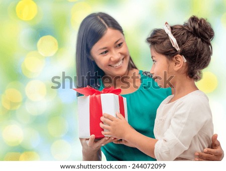 people, holidays, christmas and family concept - happy mother and daughter giving and receiving gift box over holiday green lights background