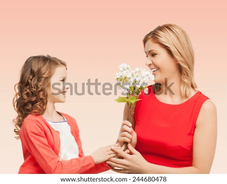 people, holidays, relations and family concept - happy little daughter giving flowers to her mother over beige background