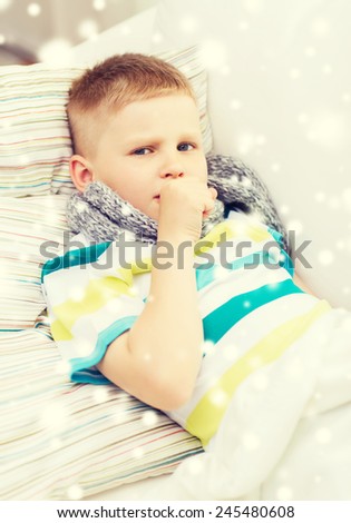 childhood, healthcare and people concept - ill boy with scarf lying in bed and coughing at home