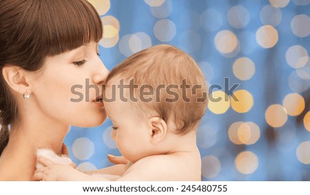 people, family, motherhood and children concept - happy mother hugging adorable baby over blue lights background