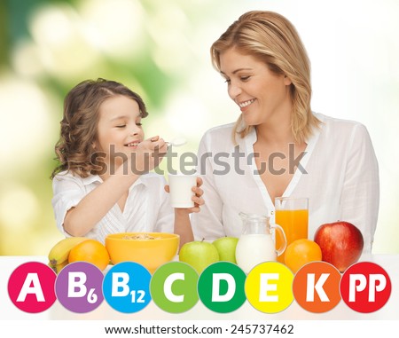 people, healthy lifestyle, family and food concept - happy mother and daughter eating healthy breakfast over green background with vitamins