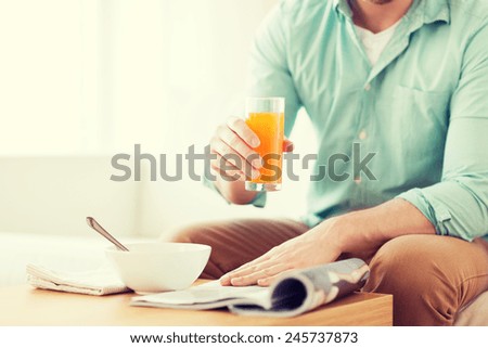 home, news, food, drinks and people concept - close up of man reading magazine and drinking juice sitting on couch at home