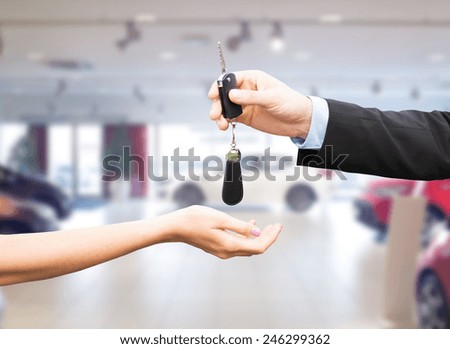 auto business, car sale, transportation, people and ownership concept - close up of car salesman giving key to new owner or customer over auto show background