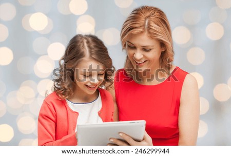 family, technology, people and christmas holidays concept - happy mother and daughter with tablet pc computer over lights background