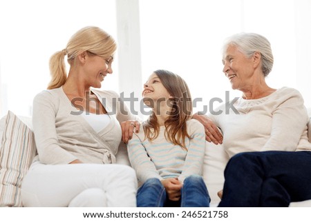 family, happiness, generation and people concept - smiling mother, daughter and grandmother sitting on couch at home