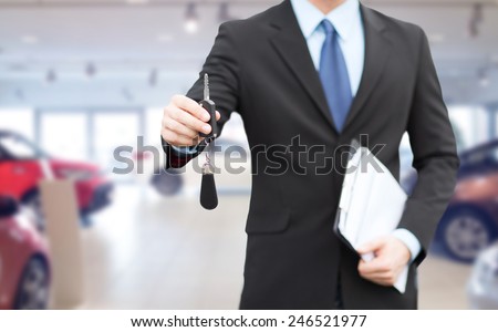 auto business, car sale, gesture and people concept - close up of businessman or salesman with documents giving car key over auto show background