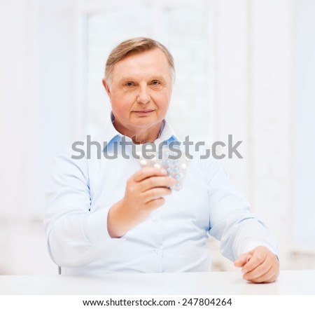 healthcare, medicine, pharmacy and elderly concept - old man with pack of pills