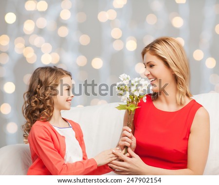 people, holidays, relations and family concept - happy little daughter giving flowers to her mother over holidays lights background