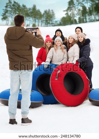 winter, leisure, sport, friendship and people concept - group of smiling friends with snow tubes taking picture by tablet pc computer outdoors