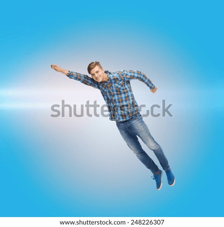 happiness, freedom, movement and people concept - smiling young man flying in air over blue background with laser light