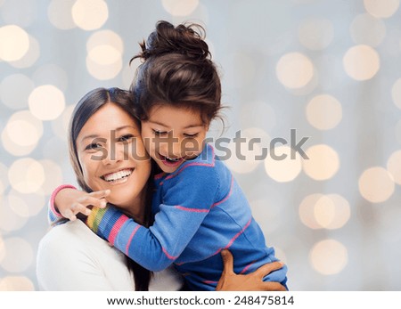 people, happiness, love, family and motherhood concept - happy mother and daughter hugging over holiday lights background