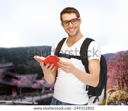 people, travel, tourism and education concept - happy young man with backpack and book travelling over asian landscape background
