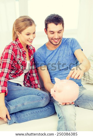 money, home, finance and relationships concept - smiling couple with piggybank sitting on sofa