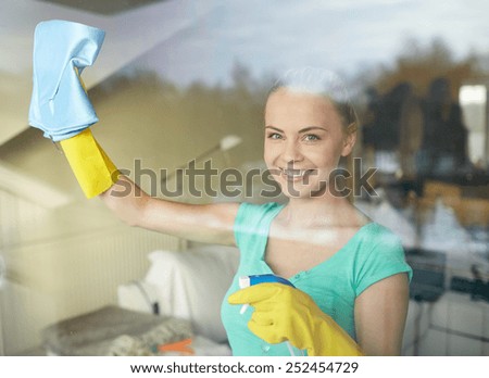 people, housework and housekeeping concept - happy woman in gloves cleaning window with rag and cleanser spray at home
