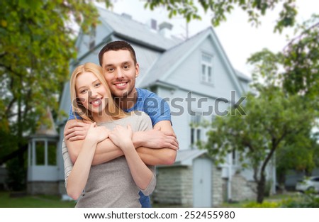 love, people, real estate, home and family concept - smiling couple hugging over house background