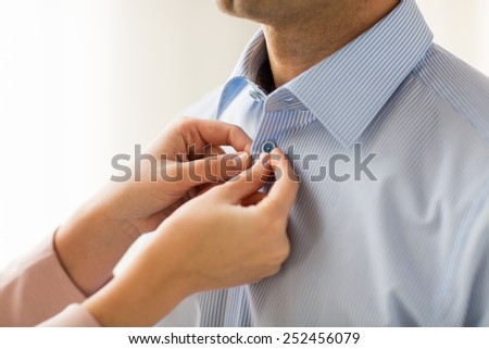 people, business, care and clothing concept - close up of woman helping man and fastening buttons on his shirt at home