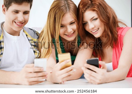 education, relationships and technology concept - three smiling students with smartphone at school