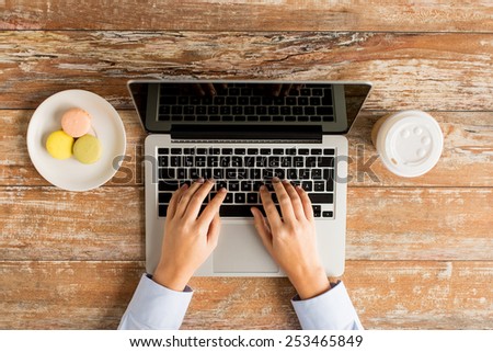 business, education, people and technology concept - close up of female hands with laptop computer, cookies and coffee cup on table