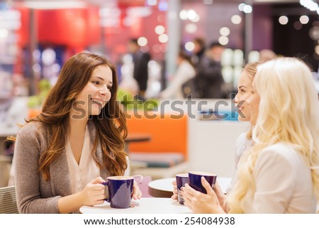 drinks, communication, friendship and people concept - happy young women with coffee cups sitting at table and talking in mall or cafe