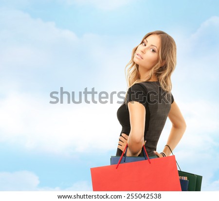people, holidays and sale concept - young happy woman with shopping bags over blue sky and cloud background
