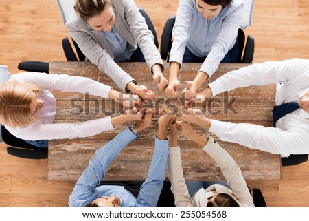 business, people and team work concept - close up of creative team showing thumbs up and sitting at table in office