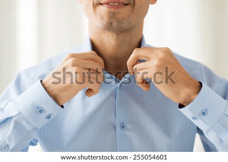 people, business, fashion and clothing concept - close up of smiling man dressing up and adjusting shirt collar at home
