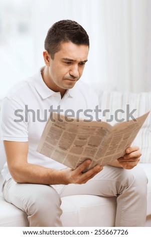 leisure, information, people and mass media concept - sad man reading newspaper at home