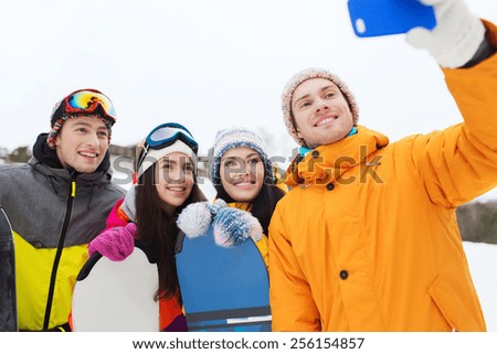 winter sport, leisure, friendship, technology and people concept - happy friends with snowboards and smartphone taking selfie