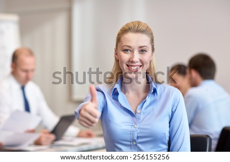 business, people, gesture and teamwork concept - smiling businesswoman showing thumbs up with group of businesspeople meeting in office