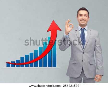 business, people, economics and financial success concept - happy smiling businessman in suit ok hand sign with growth chart over gray background