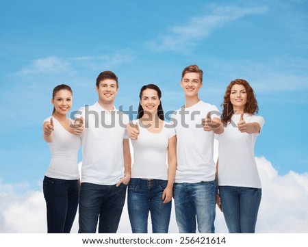 advertising, dream, future and people concept - group of smiling teenagers in white blank t-shirts showing thumbs up over blue sky with white cloud background