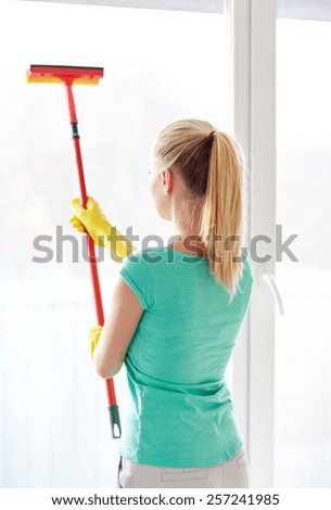 people, housework and housekeeping concept - happy woman in gloves cleaning window with sponge mop at home