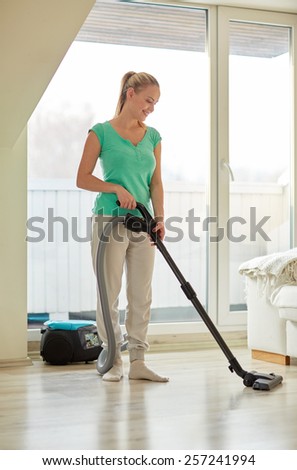 people, housework and housekeeping concept - happy woman with vacuum cleaner at home