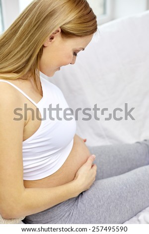 pregnancy, motherhood, people and expectation concept - close up of happy pregnant woman with bare tummy at home
