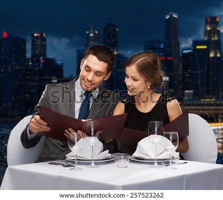 food, holidays and people concept - smiling couple with menus at restaurant over night city background